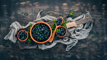 Blueberries with leaves in a wooden plate. On a wooden background. Top view. Free space for your text.