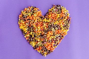 Heart shape made of colorful fusilli macaroni, on purple background. Love pasta concept.