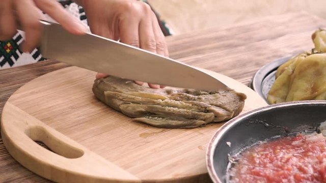 Hands of woman cutting grilled eggplant on wooden board.