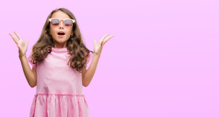 Brunette hispanic girl wearing sunglasses very happy and excited, winner expression celebrating victory screaming with big smile and raised hands