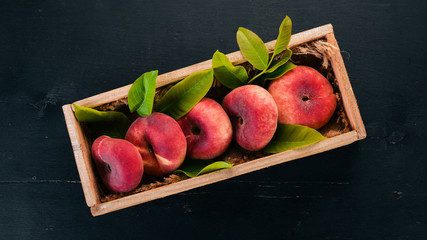 Flat peach in a wooden box. On a black wooden background. Top view. Free space for your text.