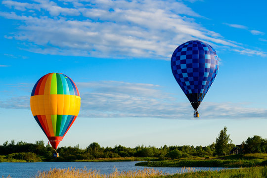 Bright colorful hot air balloons flying over lake in the clear b