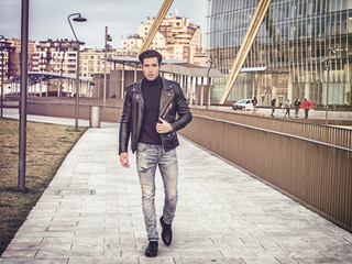 Fototapeta na wymiar One handsome young man in urban setting in modern city, standing, wearing black leather jacket and jeans