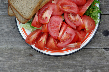 Sliced tomatoes, cucumbers, parsley, dill and bread on a plate: top view