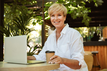 Cheerful mature woman sitting at a cafe with laptop