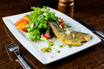 Appetizing tasty baked fish served with tomatoes, oranges and sp