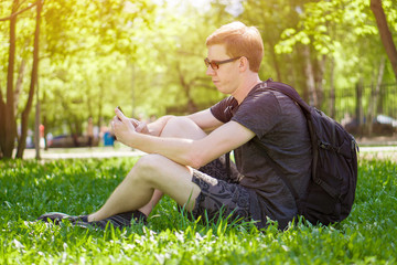 Naklejka na ściany i meble a man sits on the grass and looks at the phone