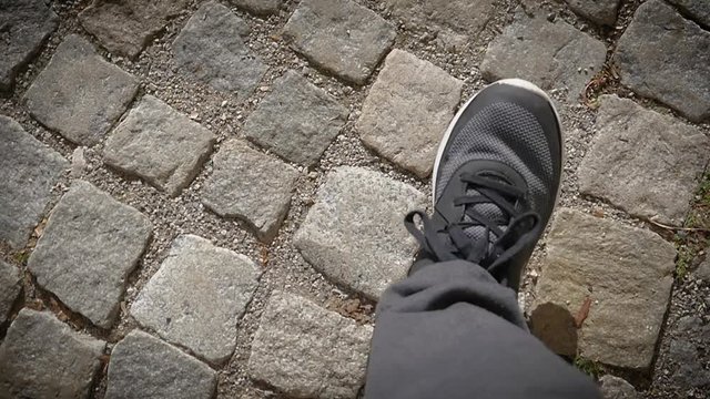 Man legs in dark sneakers walk the pavement street - upper POV camera slow motion