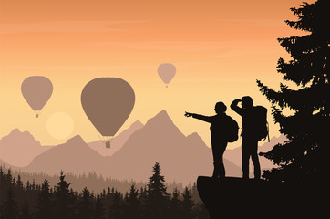 Two hikers looking down into the valley between mountains with forest and flying hot air balloons