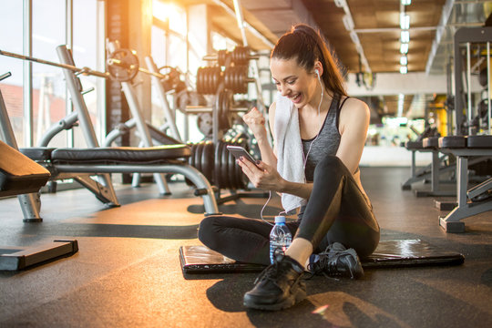 Euphoric Young Woman Reading Good News On Mobile Phone During Rest In Fitness Workout At Gym