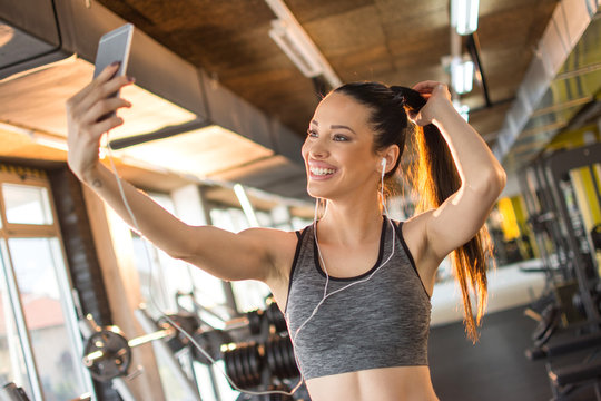 Beautiful cheerful girl in sportswear taking selfie after workout in gym