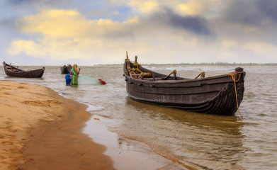 Wooden fishing boats at the beach with tribal women catching fish at Orissa coastal creek Kirtania sea beach at sunset.