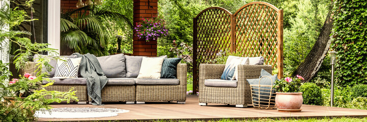 Panorama of wicker garden furniture with cozy pillows and blankets on a wooden terrace in beautiful...