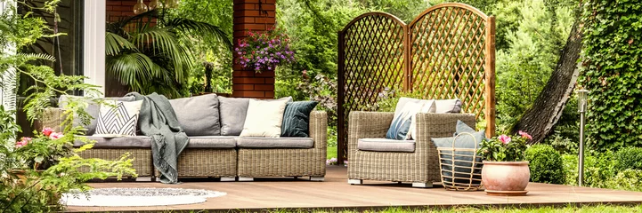 Fotobehang Panorama of wicker garden furniture with cozy pillows and blankets on a wooden terrace in beautiful outdoor greenery © Photographee.eu