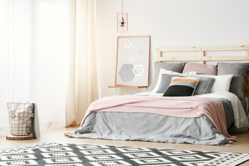 Pink blanket on grey bed in modern bedroom interior with poster and patterned carpet. Real photo