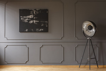 Black painting on grey wall with molding in dark apartment interior with lamp. Real photo - obrazy, fototapety, plakaty
