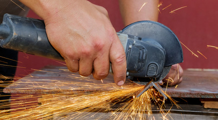 A manual angle grinder cuts metal. Sparks fly out from under the disc.