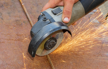 A manual angle grinder cuts metal. Sparks fly out from under the disc.