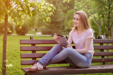 Obraz premium girl with a tablet sitting on a bench in the Park