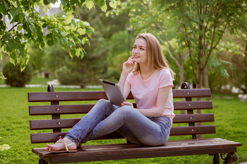 Obraz premium girl with a tablet sitting on a bench in the Park
