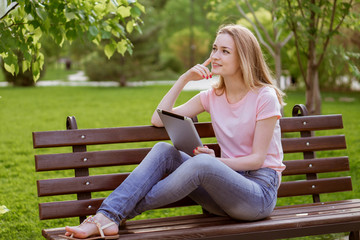 Fototapeta premium girl with a tablet sitting on a bench in the Park