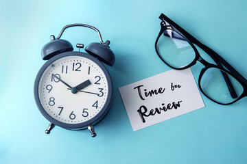 Time concept with  paper note of Time fo Review  message , alarm clock with a reading eyeglasses decoration on blue background - 213797535