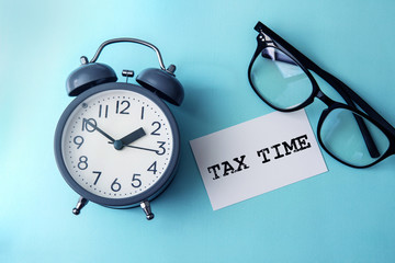 Time concept with  paper note of TAX TIME  message , alarm clock with a reading eyeglasses...