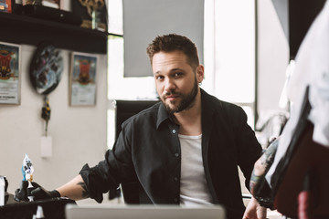 Professional tattooer dreamily looking in camera prepearing doing tattoo by tattoo machine in studio