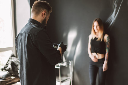 Professional tattooer taking photos on camera of tattooed girl standing on black background in modern studio
