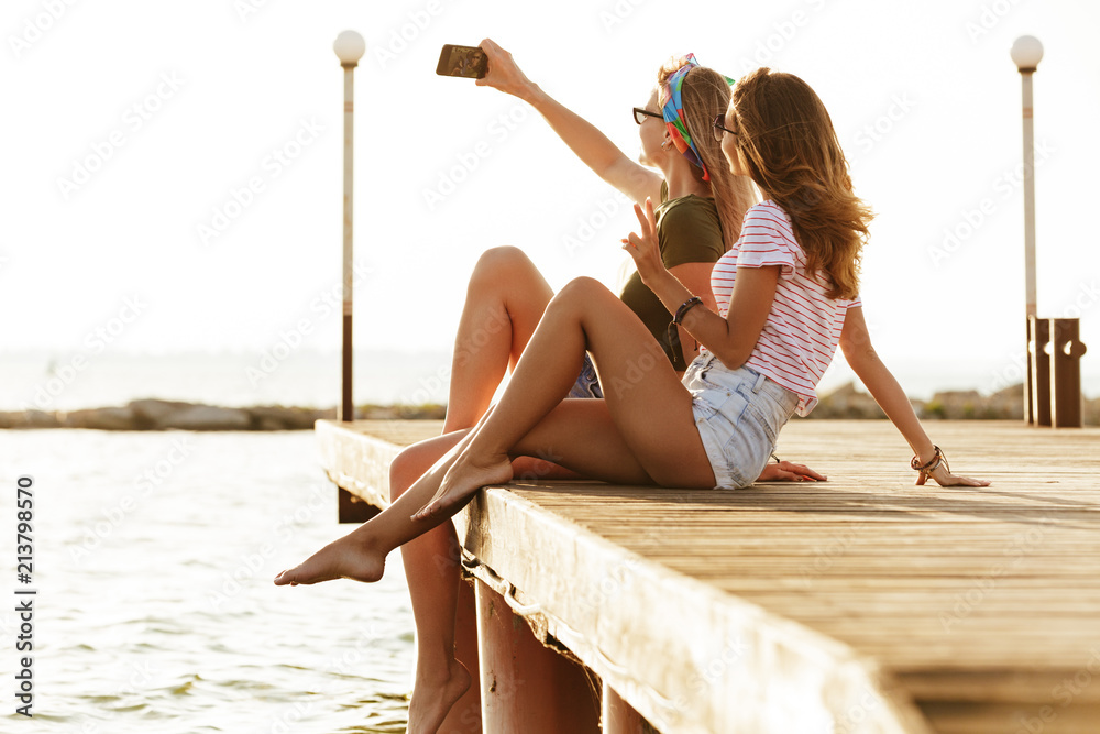 Sticker Women sitting outdoors on the beach take a selfie.