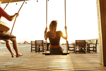 Friends outdoors on the beach riding on swing.