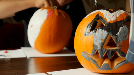 Young boy carving and painting a pumpkin for Halloween on a table