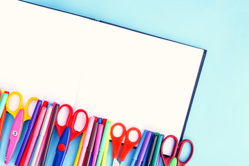 School supplies. Back to School design elements. Colorful markers and scissors on opened empty notepad on light blue paper background.