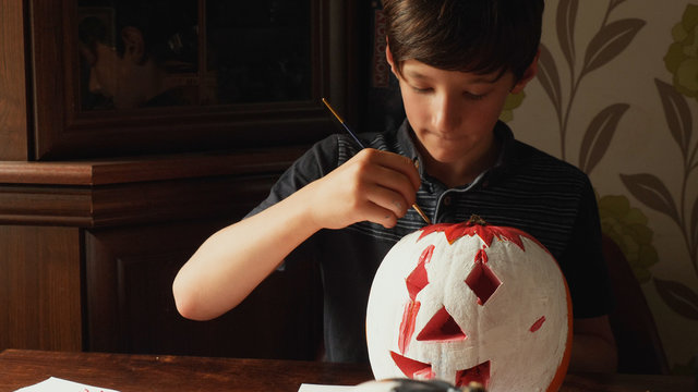 Boy carving and painting pumpkin for Halloween