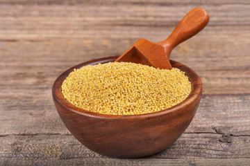 Millet in brown wooden bowl on wooden table with the spoon.
