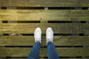 Selfie of woman feet, wear white shoe and blue jeans, stripe wood texture background, copy space for text