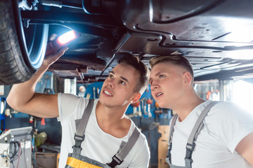Two skilled auto mechanics analyzing together the rims of a lifted car while working in a modern...