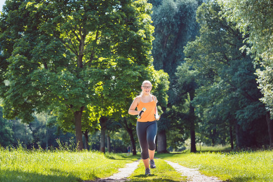 Cheerful young girl running down a path on meadow with weight dumbbells