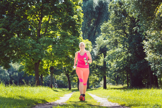 Woman running down a path on grass meadow with weight dumbbells