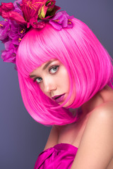 beautiful young woman with pink bob cut and flowers in hair looking at camera isolated on violet