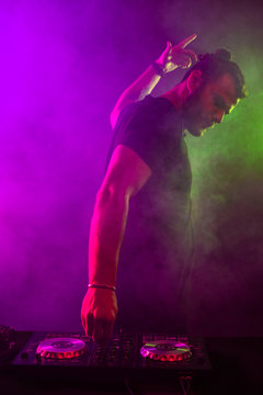 Attractive young DJ playing on turntables with color light effects