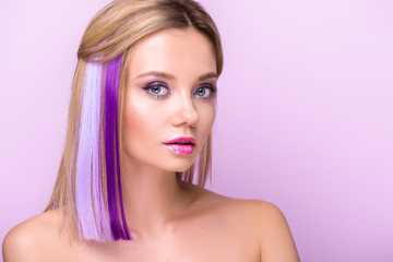 Fototapeta premium close-up portrait of stylish young woman with stylish makeup and purple hair strands looking at camera isolated on purple