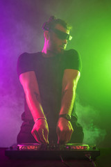 Attractive young DJ playing on turntables with color light effects