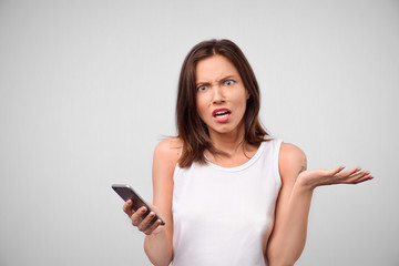 Fototapeta premium Portrait of angry and annoyed attractive female businesswoman holding smartphone and shaking palm with displeased expression, showing her anger