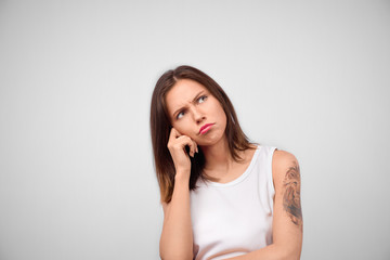 Horizontal portrait of attractive brunette female has unhappy look, thinks how to solve her problem, looks up, poses against white background with copy space
