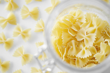 Uncooked Italian farfalle pasta, on a white background. Raw pasta is scattered around the trasparent glass. Flour products.