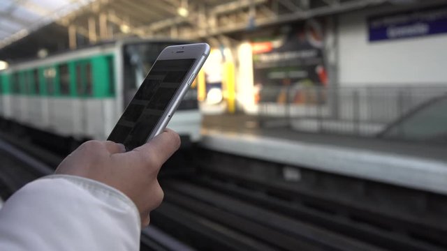 4K, Young asian woman using smartphone on active subway platform. As a train passes, girl checks social network, looking pictures on her phone device, Paris train station platform, France-Dan