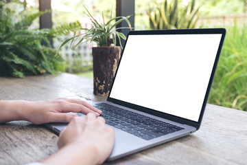 Mockup image of a woman using and typing on laptop with blank white desktop screen on wooden table and green nature background