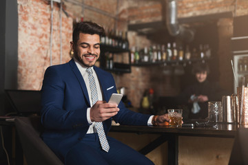 Young man sitting at bar counter and using smartphone