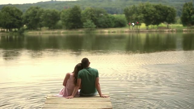 Beautiful youn couple sit on the pier near the lake